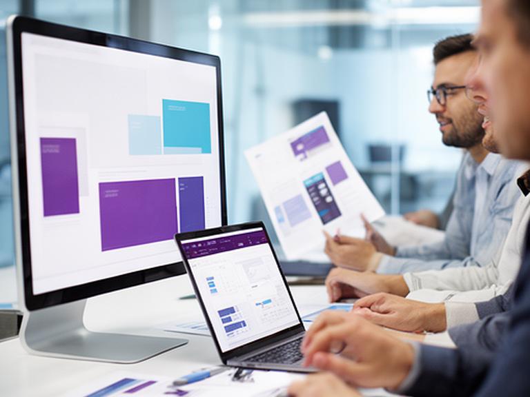 Fundadores de una empresa tecnológica revisando planos de patente y pantallas con código en una oficina moderna